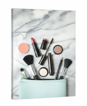 Aerial view of make up products spilling out of a pastel blue cosmetics bag, on a white marble counter top background