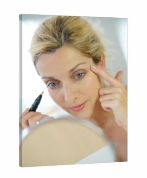 Middle-aged blond woman putting eye concealer in front of mirror