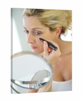 Middle-aged blond woman putting eye concealer in front of mirror