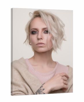 Portrait of girl of blonde with dark eye makeup and short hair in a light pink sweater standing on a light background looking into the camera, the photo below