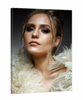 Young blonde girl with hairdo and creative makeup. Beautiful model in a fur coat. Shining skin. Evening image. Beauty of the face. Photo is taken in the studio.