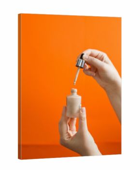 Woman puts a liquid foundation out of a bottle on orange background