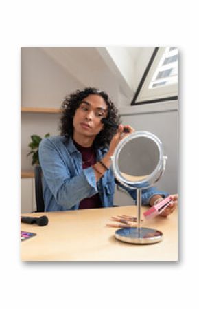 Non-binary person applying makeup with brush at loft desk near round mirror by skylight, copy space