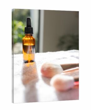 Amber dropper bottle resting on white towel with condensation in window light beside makeup brushes