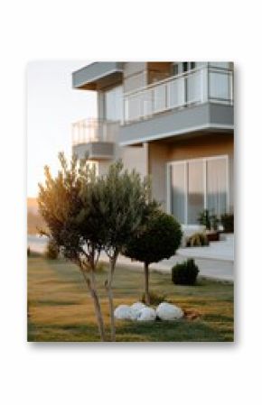 Golden light bathes a contemporary building set in a manicured garden. Neatly trimmed trees add elegance to the tranquil outdoor space just before dusk.