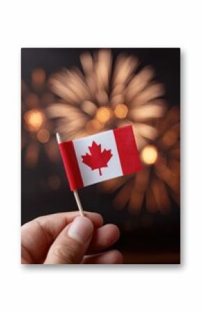 Small Canadian flag held against backdrop of vibrant fireworks,