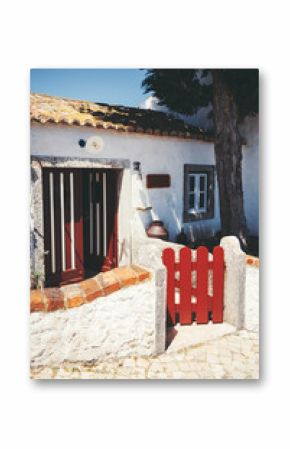Charming traditional Portuguese countryside house in Aldeia da Mata Pequena, with whitewashed walls, red wooden gate, rustic tiled roof and cobblestone path in warm afternoon sunlight