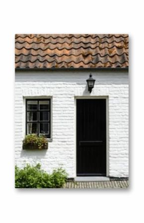 Charming white house with black door and window surrounded by greenery in a quaint village setting during daylight hours