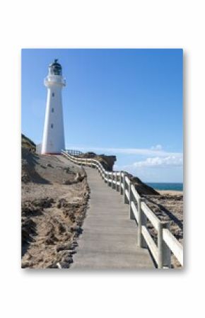 Castlepoint Lighthouse stands tall against a clear blue sky in New Zealand. A walkway leads to the iconic landmark, guiding visitors to experience its beauty.