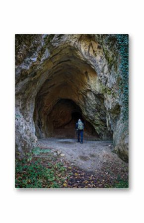 A lone hiker with trekking gear stands at the wide entrance of Büdös-pest Cave, a prehistoric site in the Bükk Mountains, Hungary.