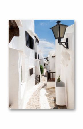 Charming narrow cobblestone street with traditional whitewashed houses and dark wooden shutters in the fishing village of Binibeca Vell, Menorca, Spain, bathed in sunlight