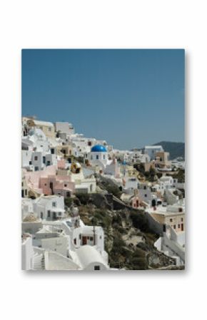 Vertical shot of the whitewashed houses and blue domes of Oia, Santorini, under a clear blue sky. A classic example of Cycladic architecture on a stunning Greek island cliffside.