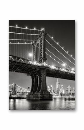 New York City black and white night view of the Manhattan Bridge from DUMBO. Illuminated Lower Manhattan skyline with skyscrapers reflected on the East River