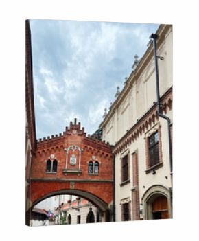 Red brick archway in a historic European street with pedestrians and buildings in Krakow, Poland.