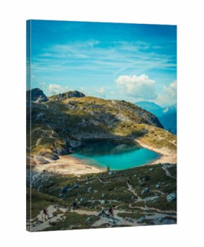 Aerial view of bright turquoise alpine lake surrounded by rocky peaks and hiking trails in the Italian Alps