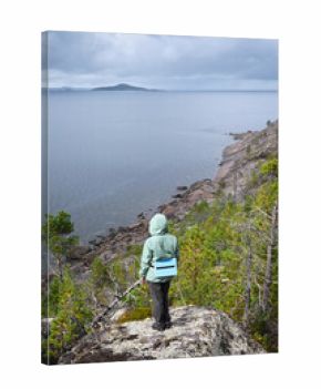 Person in green jacket overlooking rocky shoreline under overcast sky in White Sea, Karelia, Russian North, nature and travel concept