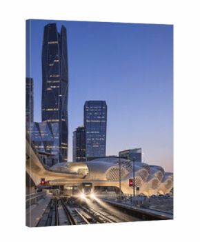 Riyadh Metro futuristic station architecture with train and KAFD towers in Saudi Arabia at twilight