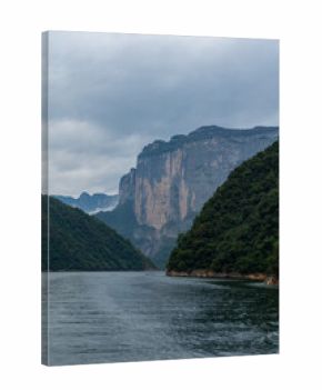 Enshi City, China mountains rise above the calm river water as clouds gather in the sky creating a majestic landscape view.