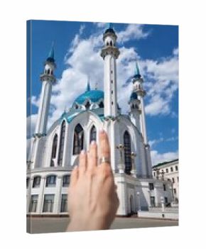 Russia,Kazan, Kul Sharif Mosque, 20.06.2022The grand white and blue Kul Sharif Mosque under a sunny sky, with a person's hand reaching towards a minaret.