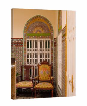 Traditional Tangier house interior with patterned tiles, ornate window, wooden chairs and historic Moroccan design elements.