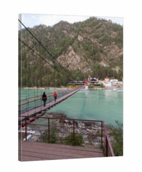A suspension bridge spans a turquoise river, guiding travelers toward a mountain village