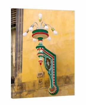 Colorful Ornate Street Lamp With Green Red Details Mounted on Yellow Stucco Wall Historic Facade