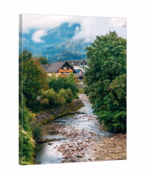 Mostnica river flowing through Stara Fuzina village in Bohinj valley, surrounded by traditional alpine houses and mountain landscape.