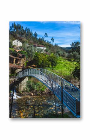 rural scene featuring a metal footbridge that spans a gently flowing stream, connecting lush green fields on both sides