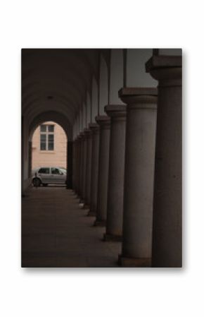 A view down a long historical arcade or colonnade, characterized by a repeating series of arches supported by substantial columns, which create a strong sense of linear perspective