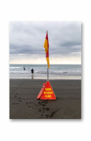 Swimmers and surfers stay safe by swimming between the flags on a beach in New Zealand, marked by Surf Life Saving. Karekare, Auckland, New Zealand