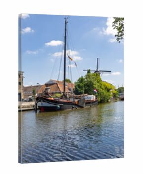 A beautiful traditional Dutch sailing barge is moored on a serene canal in Gouda, with a classic windmill visible in the background.