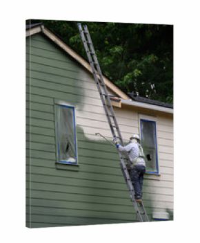 Professional painter wearing a hard hat and respirator on a ladder using a sprayer to paint the exterior of a new build house green, new housing development under construction 
