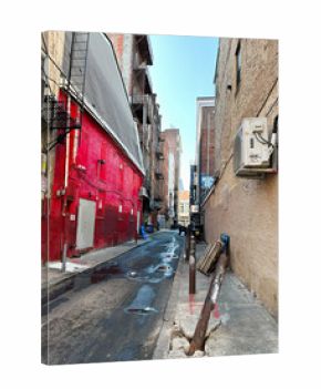 Narrow Philadelphia alley with red brick wall fire escape and wet street under clear sky