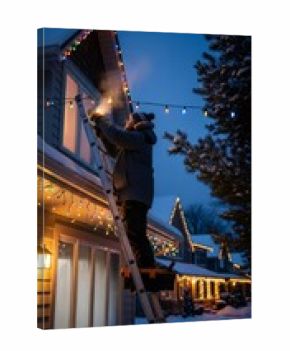 Man on ladder installing Christmas lights on house in winter night. Holiday decoration and maintenance concept for festive season.