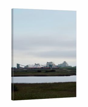 Potash factory with covered mineral piles and rail cars near a water body under cloudy skies in Saskatchewan, Canada.