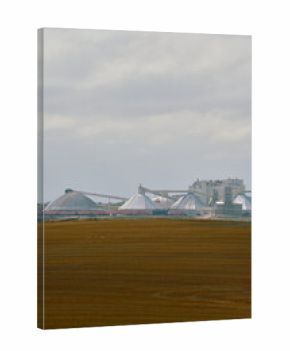 A potash plant with multiple dome-shaped storage buildings and conveyors viewed across farmland under cloudy skies in Saskatchewan, Canada.