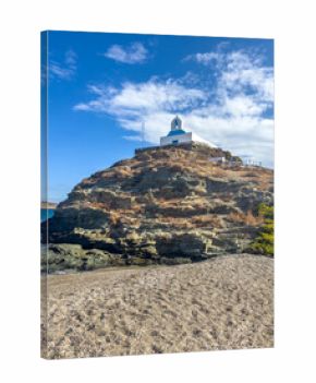 Whitewashed St George Church stands upon the rocky hill above a quiet beach on Kea island, also known as Tzia, under bright midday sunlight featuring blue sky 