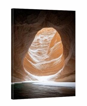 A view from inside a dark canyon, looking out towards a brightly lit opening. A river flows in the foreground, with snow lining its banks and the canyon walls.