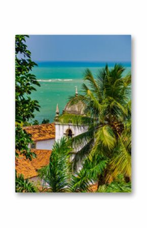 Baroque church tower hidden between vegetation and the sea in the historic city of Olinda in Pernambuco