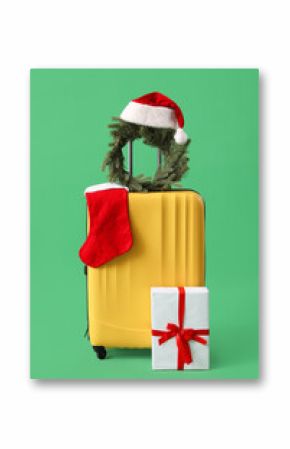 Suitcase with Christmas wreath, Santa hat, sock and gift on green background