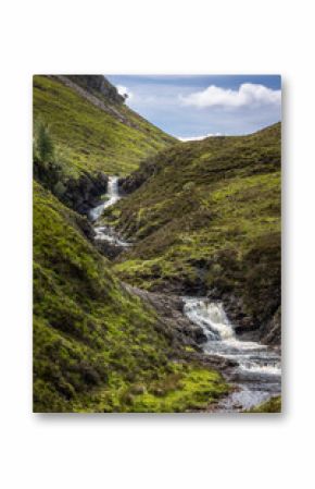 Typical Scottish landscape with hills, rocks, a cloudy blue sky and the many rivers, waterfalls and lochs in the Scottish highlands.