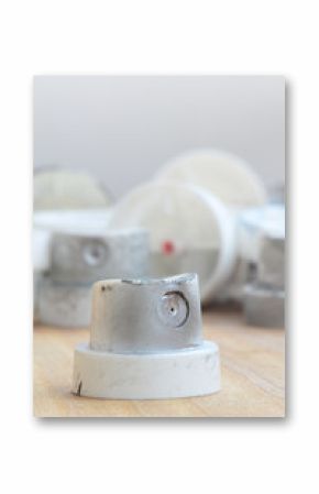 Several plastic nozzles from a paint sprayer that lie on a wooden surface against a gray wall background. The caps are smeared in chrome paint. The concept of street art and graffiti