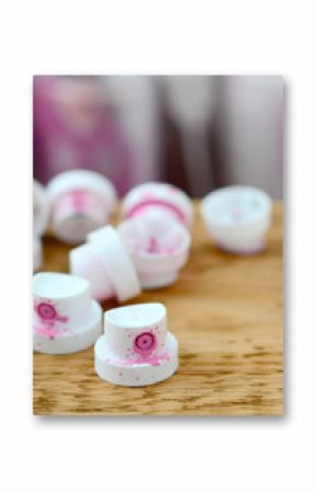 The soiled pink nozzles from the paint sprayer lies on a wooden plank on a background of a many dirty spray cans