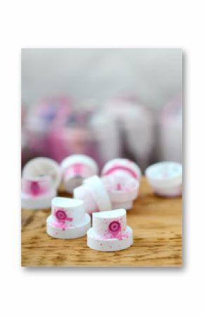 The soiled pink nozzles from the paint sprayer lies on a wooden plank on a background of a many dirty spray cans