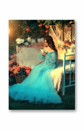 Fairy tale princess sits on white bed. Fantasy woman holding cup in hands drinking tea. Long wave hair. Blue vintage luxury royal dress. Backdrop blooming peony flowers, old lamp. Fantasy woman queen.