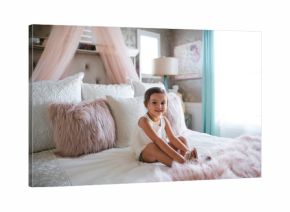 Young little girl sitting on pink princess bed in her room