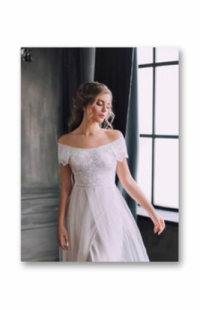 mysterious pretty lady with blond curly hair looks down modestly, enchanted girl in chic light white long vintage dress with open shoulders in dark cloak, princess in gothic castle with large windows.