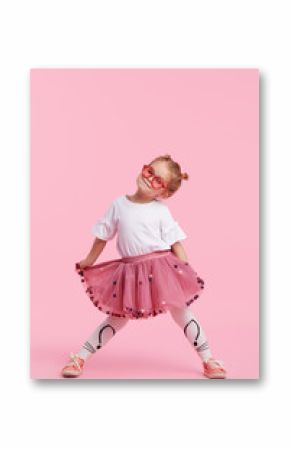 Happy childhood. Funny child girl in tulle skirt jumping and having fun isolated on pink background. Celebrating a vibrant carnival for kids, birthday party. True emotions. Space for text