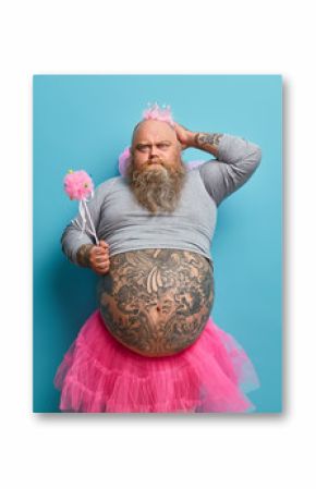 Fathers day holiday. Serious funny dad with big belly, wears princess outfit, holds magic wand, receieves congratulations from children, isolated over blue background. Playful male fairy indoor