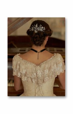 Back view of classic young lady wearing lace dress with pearls in hair playing grand piano in elegant interior, copy space